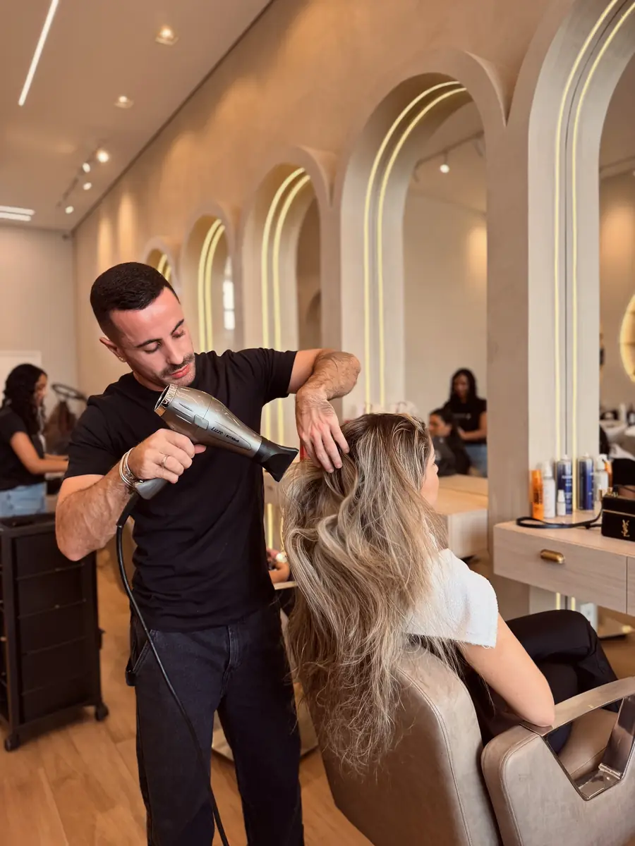 Profissional secando e modelando o cabelo de uma cliente diante dos espelhos em arco